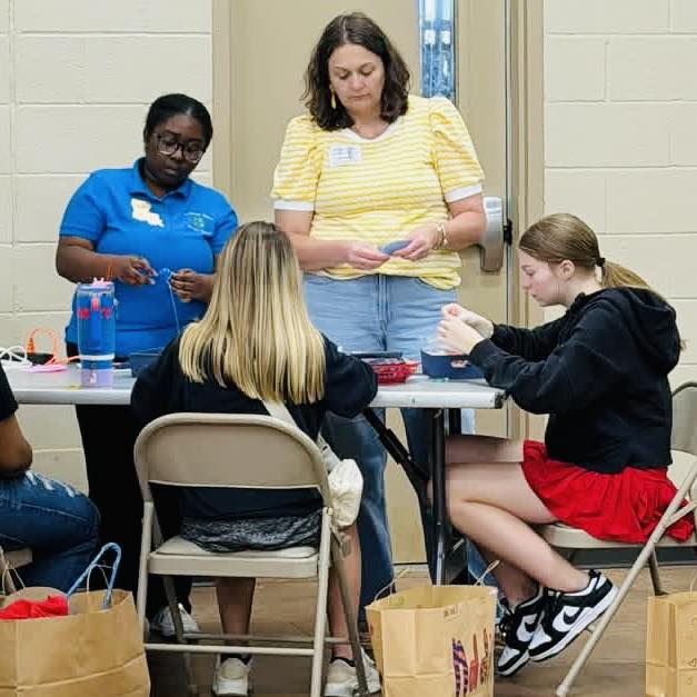 A woman and a girl standing at a table where two girls are sitting.